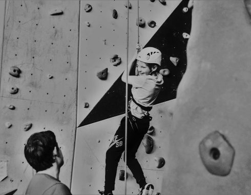 Kind an Kletterwand, dass von einem Erwachsenen gesichert wird